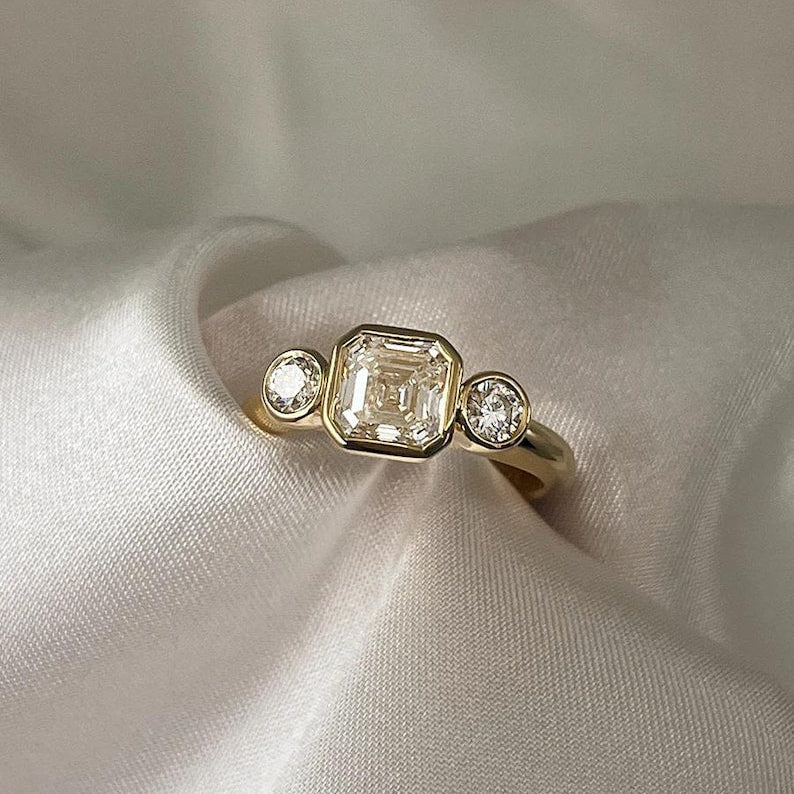 Asscher Cut Trilogy Diamond Engagement Ring featuring a 1.5ct IGI Certified Asscher Cut Lab Grown Diamond with round lab grown diamond side stones in solid gold. Three-stone engagement ring with 1.82ct total carat weight.