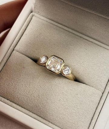 Asscher Cut Trilogy Diamond Engagement Ring featuring a 1.5ct IGI Certified Asscher Cut Lab Grown Diamond with round lab grown diamond side stones in solid gold. Three-stone engagement ring with 1.82ct total carat weight.