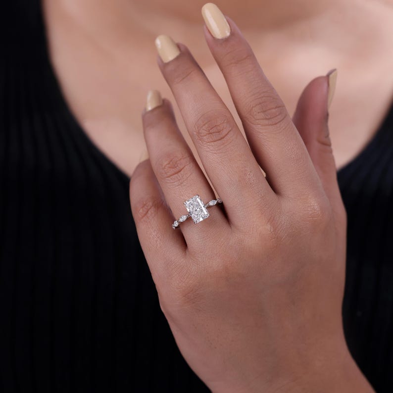 Lab grown radiant cut diamond engagement ring set in claw prong with marquise side stone created in 10k gold.
