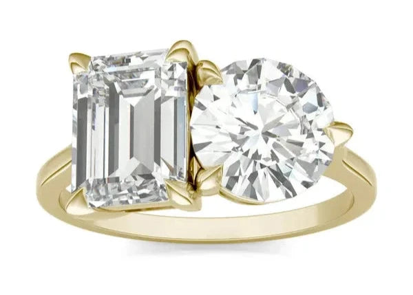 A round brilliant and emerald Toi et Moi engagement ring with a gold band, featuring two emerald stones of different sizes.