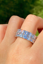 Load image into Gallery viewer, Ring with blue gemstones on a finger against a blurred green background